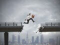 Business man jumping over broken bridge